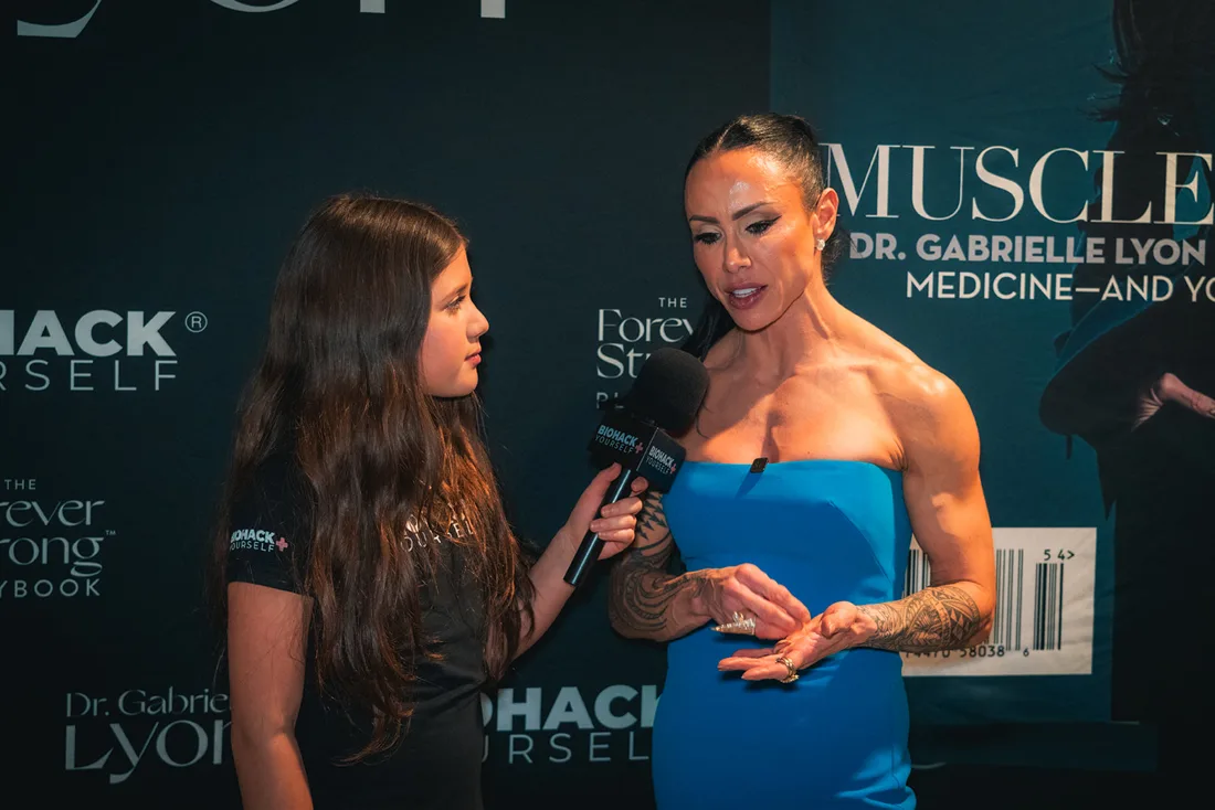 A journalist interviewing Dr. Gabrielle Lyon on the branded wall